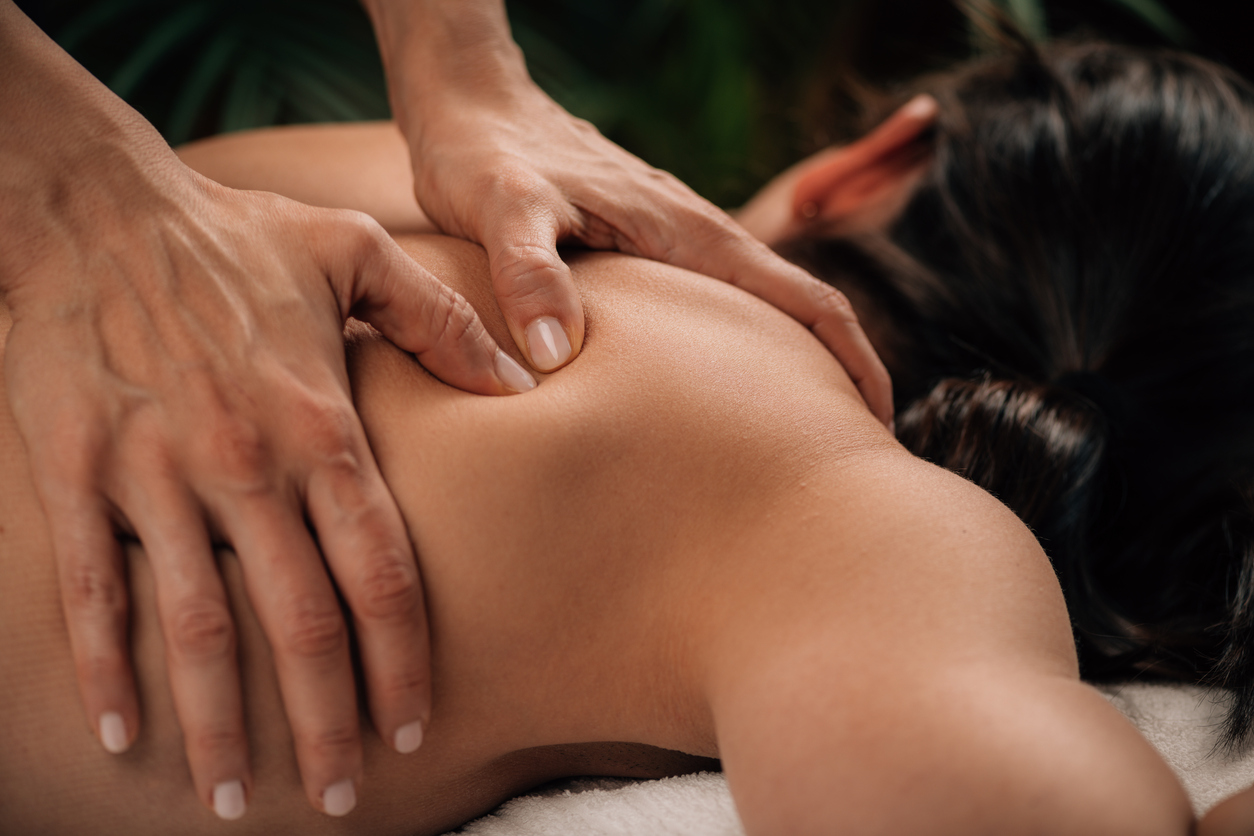 Closeup of a person receiving a back massage on a massage table. Hands applying pressure to mid-back. No face visible.